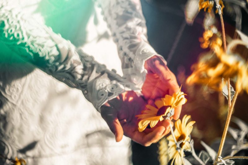 Bride's hands holding a sunflower showing details of wedding dress