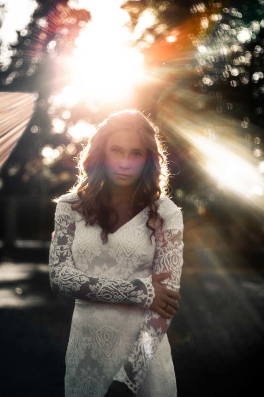 Bride standing in forest with rays of light overhead