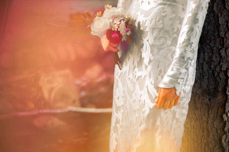 Bride holding a bouquet of flowers next to her waist, detailing the wedding dress lace